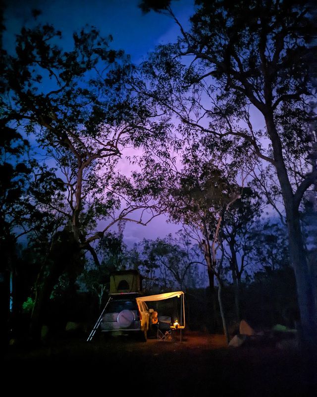 Person camping in a caravan under a purple sky in litchfield national park