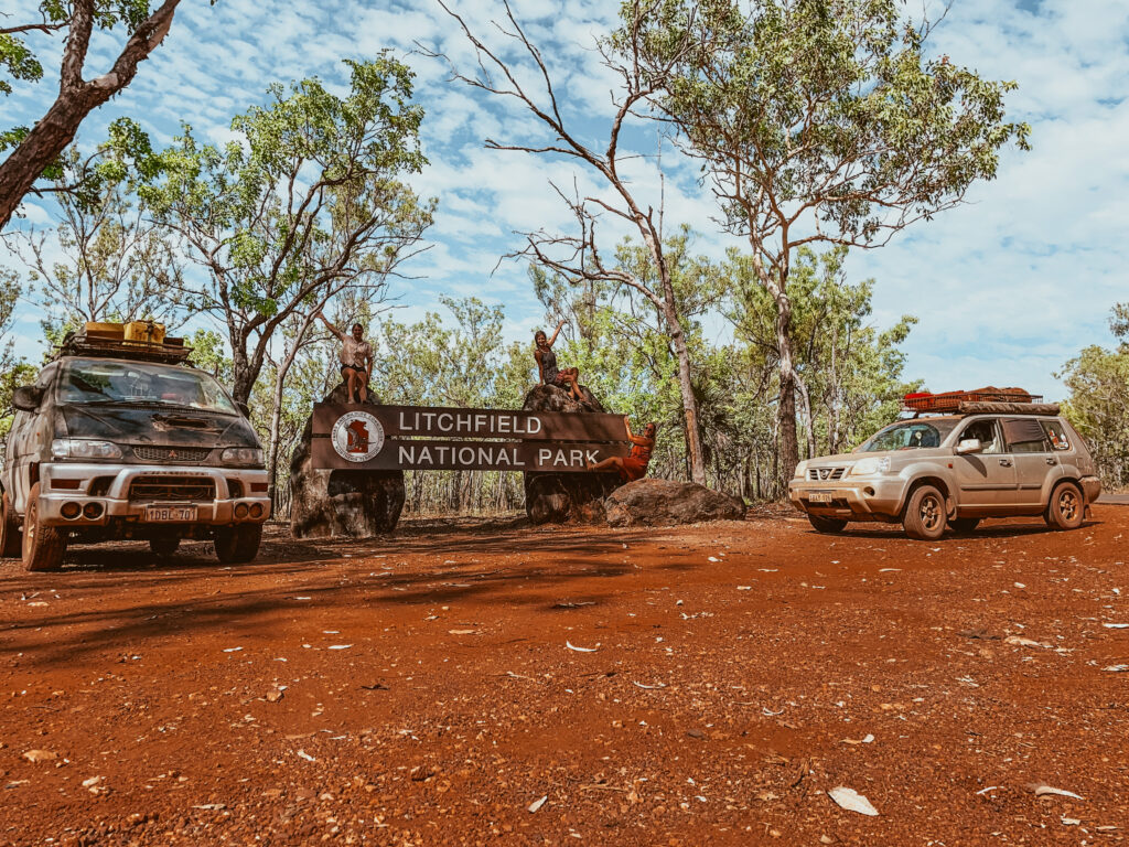 Two cars parked next to a Litchfield national park sign, couple sitting on the Litchy sign